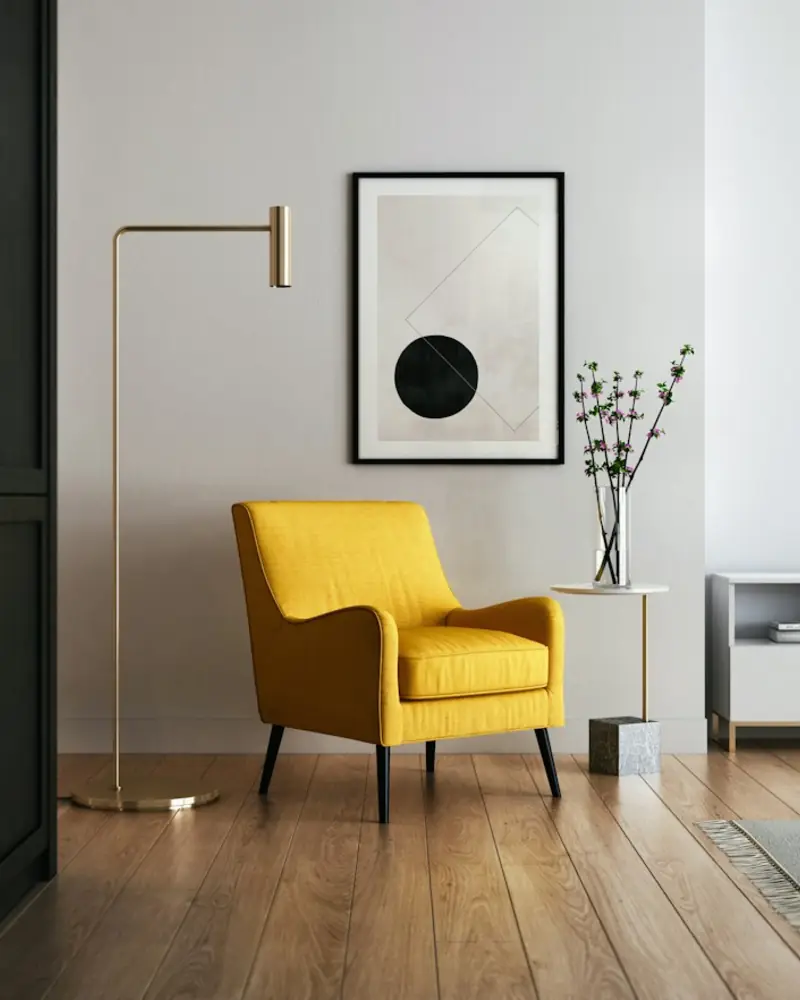 Poltrona amarela sobre piso de madeira, ao lado de um quadro minimalista