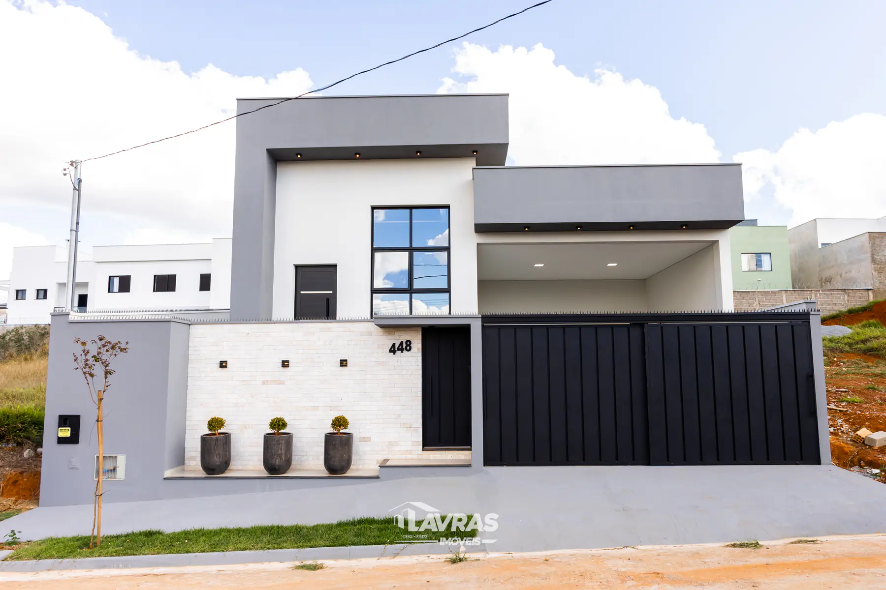 Fachada contemporânea em volumes brancos e cinza, com portão em lâminas escuras